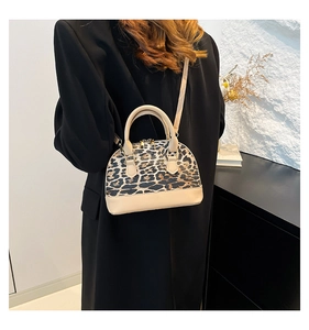 Chic leopard print dome bag with beige leather trim worn by a model in a black suit