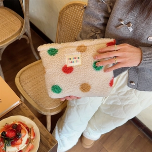 Plush beige makeup bag with colorful polka dots held in a cozy cafe setting