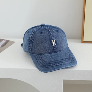 Detail view of denim baseball cap showing white H embroidery and fabric texture