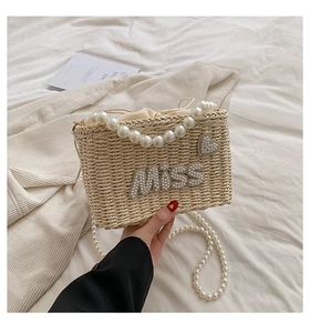 Detail of beige woven straw bag featuring pearl top handle and Miss pearl lettering