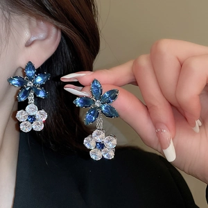 Detailed view of floral zircon earrings with blue and white crystals on a model