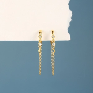 Detail of golden moon earrings with chain tassels and cubic zirconia on blue background