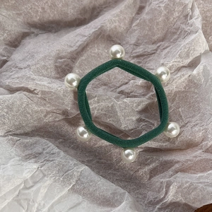 Detail of dark green elastic hair tie featuring six decorative faux pearls on textured paper