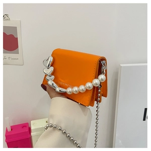 Detail of orange mini square bag with heart metal and pearl handle on white background