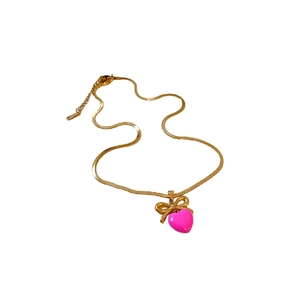 Collier en acier titane avec nœud doré et pendentif cœur rose sur fond blanc pur