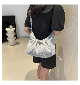 Detail view of a light gray pleated crossbody tote bag worn by a model in a modern room