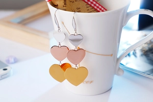 Close-up of three-tone gold heart drop earrings hanging on a white porcelain cup