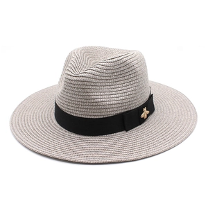 Detail of straw fedora hat featuring a black grosgrain ribbon and golden bee ornament