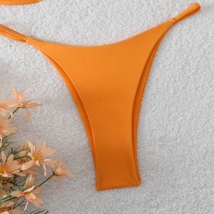 Flat lay of bright orange bikini bottom with side ties on a white faux fur background