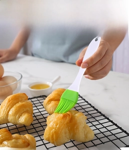 Action shot of a green silicone pastry brush spreading oil on fresh croissants on marble