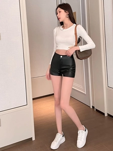 Enges weißes Crop Top und schwarze Kunstleder-Shorts mit hoher Taille und Sneakern