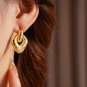 Close-up of golden textured hoop earrings with pavé diamond accents worn by a model