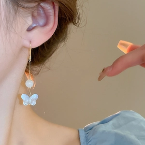 Détail de boucle d'oreille papillon blanc avec perle sur le profil du modèle