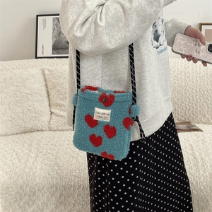 Close-up of blue plush mini bag with red heart patterns and woven shoulder strap