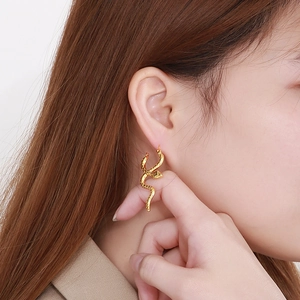 Macro shot of gold-plated snake earrings featuring detailed scale texture on a model