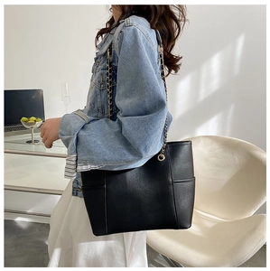 Side view of large black tote bag with gold chain strap on female model in natural light