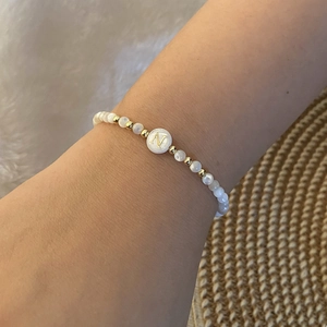 Close-up of a pearl and gold beaded bracelet with an engraved letter N charm on a wrist
