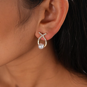 Close-up of golden X-shaped earrings with micro-set zircons and white pearl on model ear