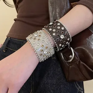 Bracelets larges en cuir avec strass et clous portés par un mannequin en tenue denim