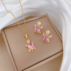 Close-up of pink crystal turtle necklace and earrings set on elegant beige jewelry box