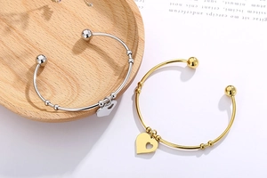 Detailed shot of polished gold and silver heart pendant open bangles on wooden decor