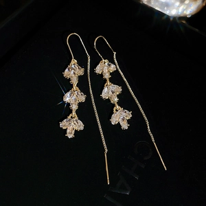 Macro shot of long gold earrings with marquise-cut zircons and leaf design detail