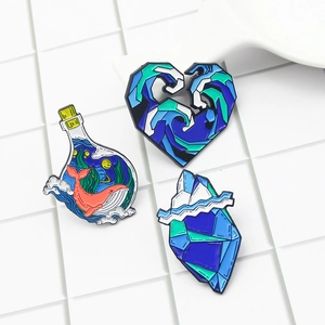 Detailed view of three ocean-themed enamel pins with whale and wave designs on a grid background