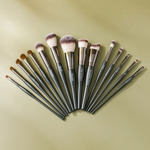 Macro shot of 14 professional black makeup brushes fanned out against a green background