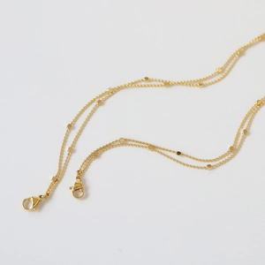 Detailed close-up of a dual-layer gold beaded chain with square accents and lobster clasps