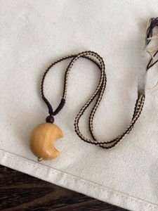 Close-up of crescent wood pendant on woven cord over rustic linen background
