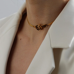 Gros plan d'un collier ras du cou doré style boucle de ceinture porté sur un tailleur blanc
