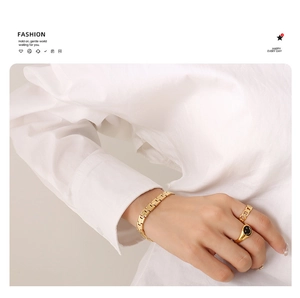 Close-up of gold chain bracelet and smiley signet ring on model's hand with white shirt