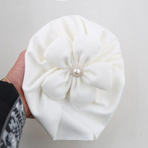 Macro shot of white infant turban hat with large cloth flower and pearl bead center