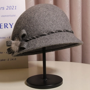 Detail of grey wool cloche hat featuring a plush fur pompom and elegant bow decoration