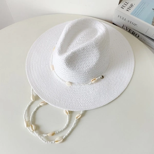 Detail of white straw sun hat featuring decorative sea shells and beaded lanyard