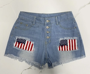Detail of light blue denim shorts with star-stripe patches and fringed hems
