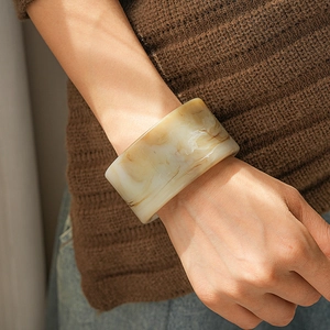 Macro detail of wide resin bangle with vintage marble texture worn on a brown knit sleeve