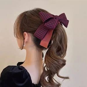 Detailed view of a burgundy houndstooth bow hair clip on a brunette wavy ponytail