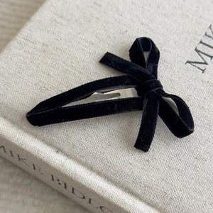 Close-up of a black velvet hollow bow hair clip on a beige book cover with soft lighting