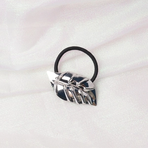 Detail of a black elastic hair tie with a shiny silver metal leaf charm on textured fabric