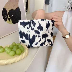 Close-up of a canvas pouch featuring black and white cow print and a woven logo label