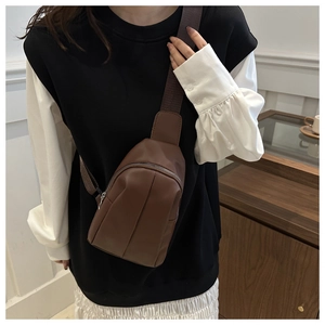 Detail of dark brown leather crossbody bag showing vertical pleats and fabric strap