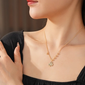 Close-up of golden clover pendant necklace with beaded chain on female model neck