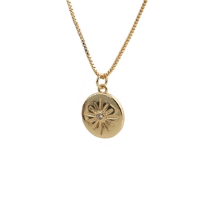 Détail du pendentif pièce dorée avec une pierre précieuse et un motif rayon de soleil