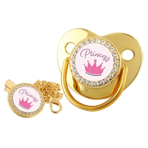 Detailed view of a golden baby pacifier with rhinestones, crown pattern and Princess text