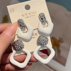 Set of two white enamel geometric drop earrings with hammered silver texture and metal accents