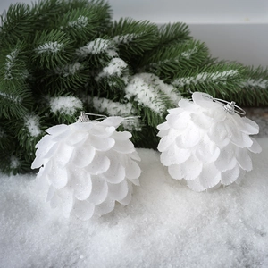 White petal Christmas balls with glitter finish and silver string on snowy pine branch