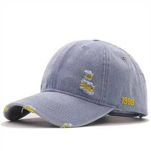Detail of yellow 1999 embroidery and distressed holes on washed blue denim baseball cap