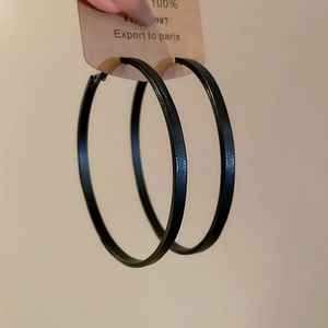 Detail view of large black vintage leopard print hoop earrings held against a plain wall