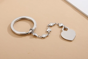 Polished silver heart pendant on a chain and round key ring on a beige surface
